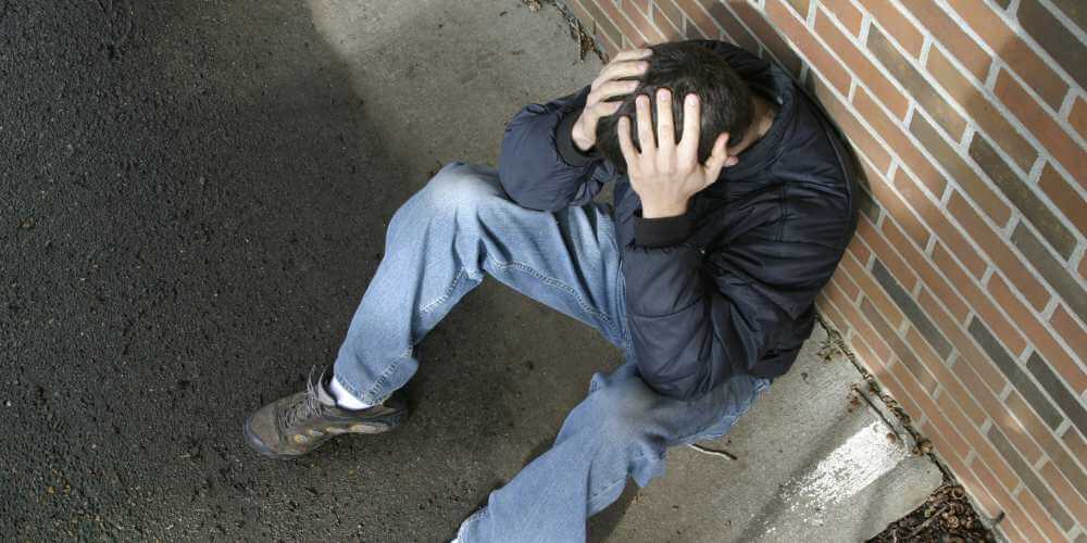 Mann sitzt mit Kopf in den Händen auf einer Bank – Symbol für Ratlosigkeit und innere Leere in einer Sinnkrise